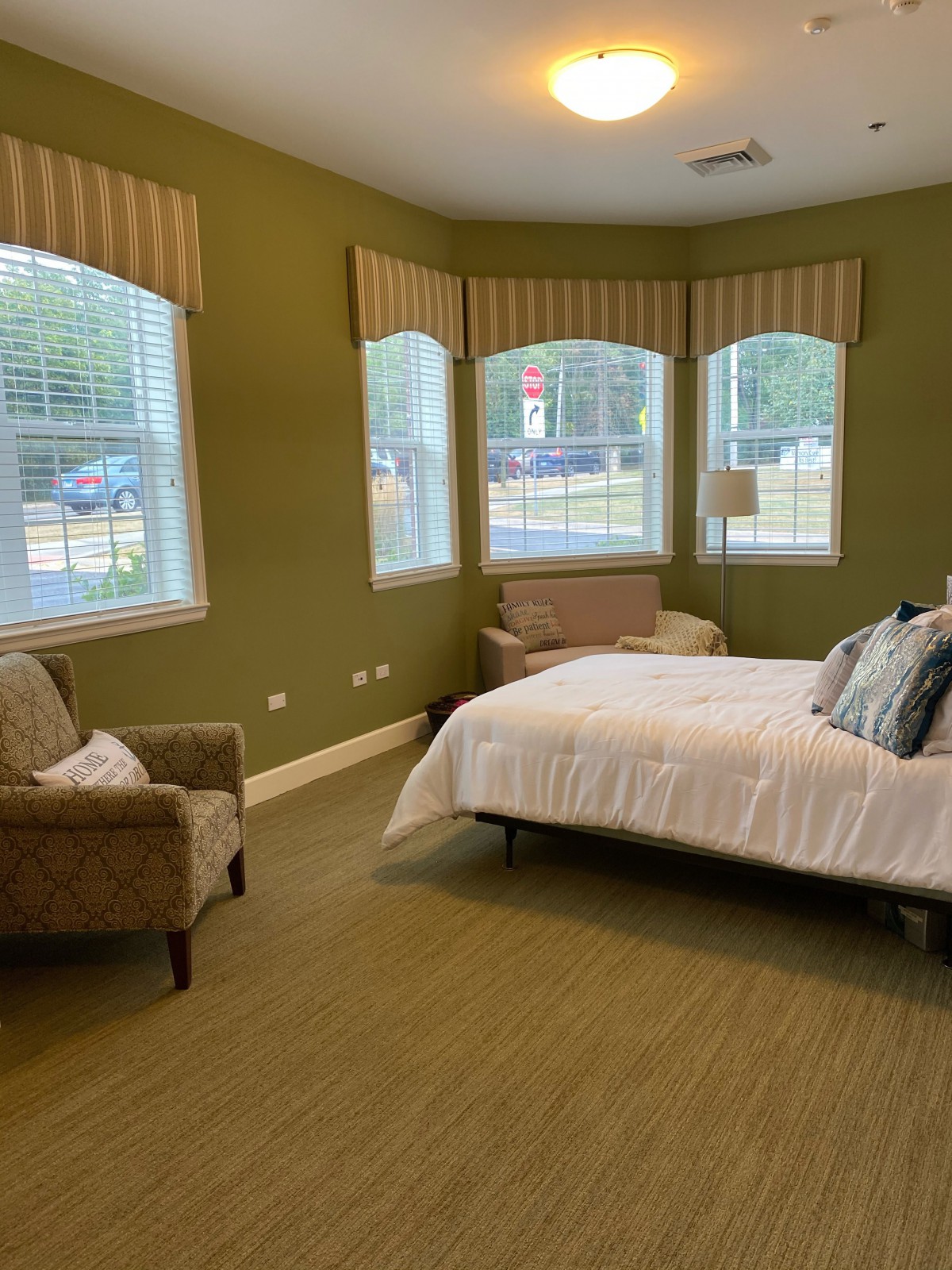 A cozy bedroom with green walls featuring a bed, armchair, and multiple windows allowing natural light.