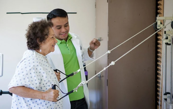 A healthcare professional assists an elderly woman during a physical therapy session.