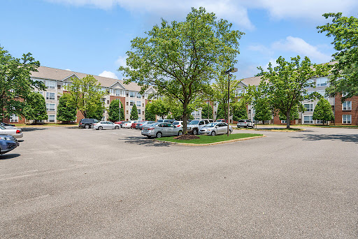 A peaceful residential parking lot surrounded by greenery and buildings under a partly cloudy sky.