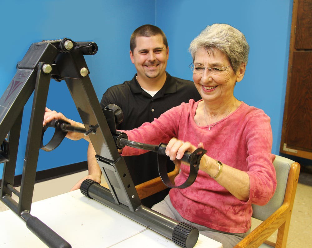 An elderly woman engaging in physical therapy with the assistance of a trainer.