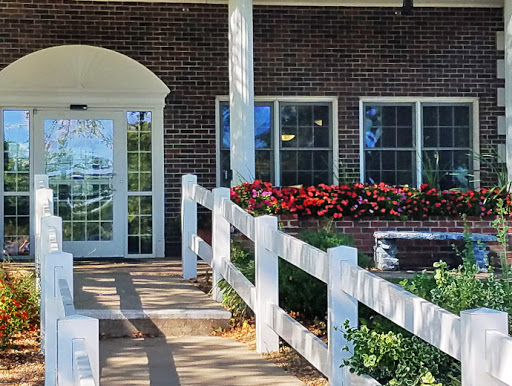 A charming entrance to a building adorned with vibrant flowers and a white fence.