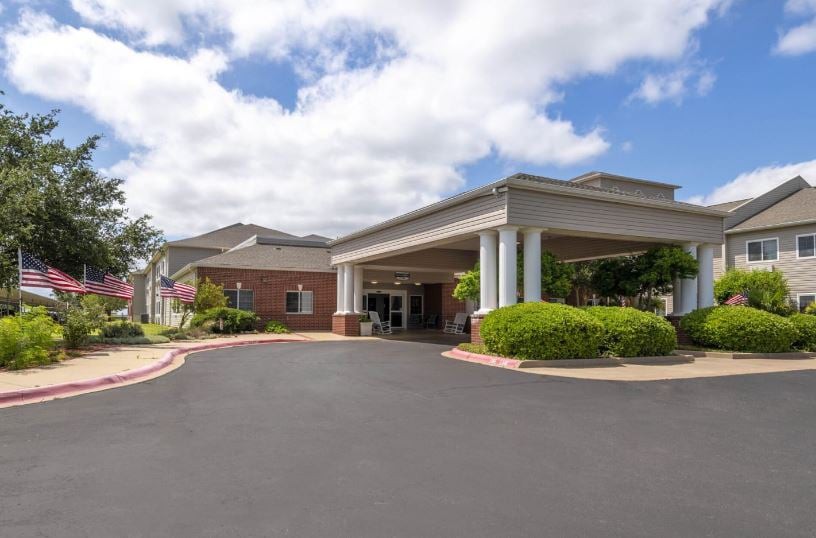 A well-maintained building entrance with a covered driveway set against a partly cloudy sky.