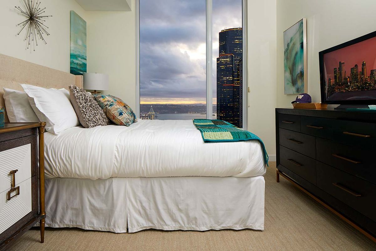 A cozy bedroom with a bed, decorative pillows, and a window offering a cityscape view.