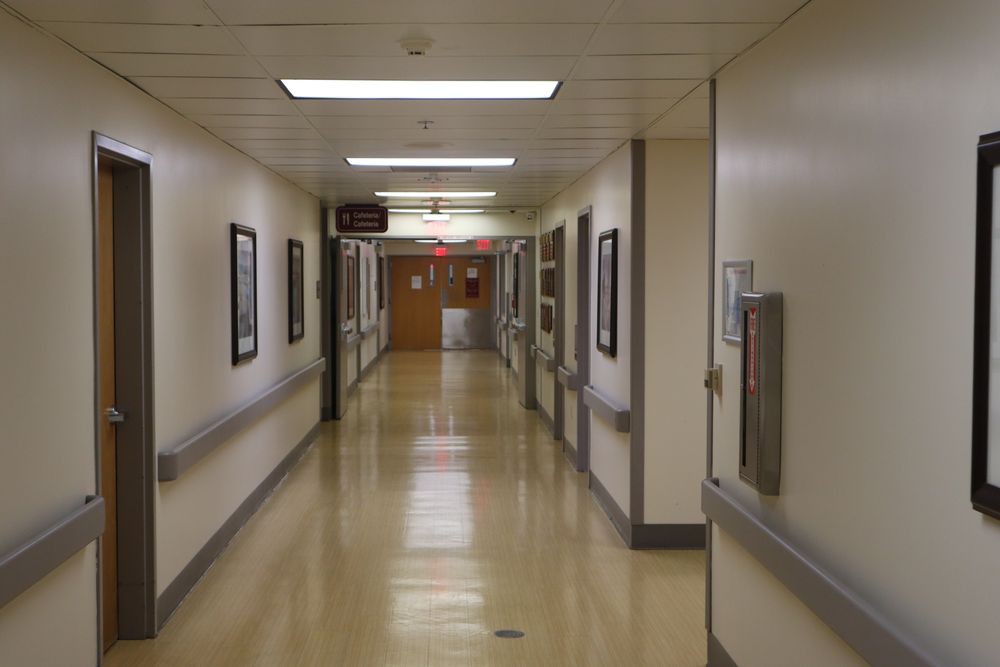 A quiet hospital corridor with fluorescent lighting and framed pictures on the walls.