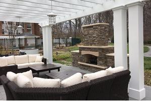 A cozy outdoor patio area with cushioned seating and a stone fireplace under a pergola.