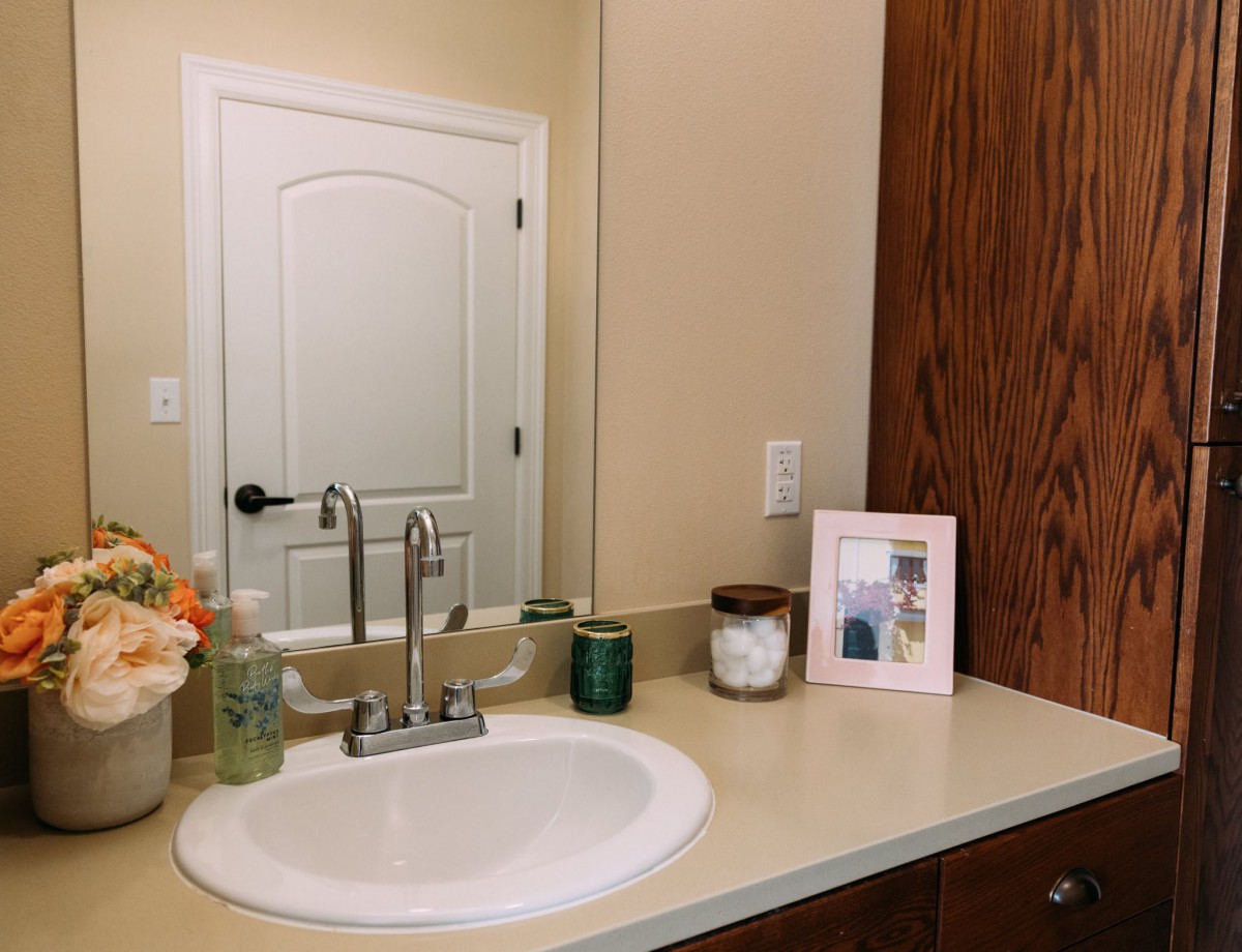 A bathroom countertop featuring a sink, mirror, and various decor items including a photo frame, candles, and a plant.