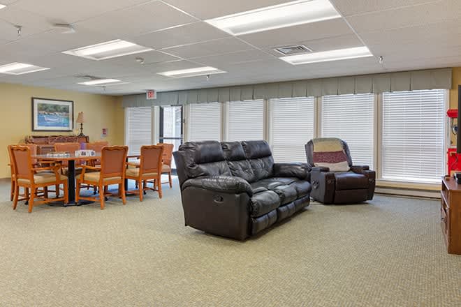 A spacious living room with a black sofa, recliner, and a dining area featuring several chairs.