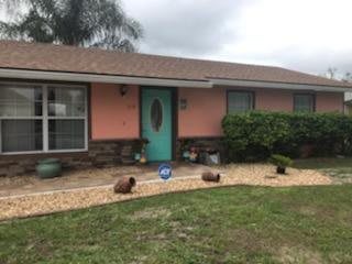 A pink house with a turquoise front door, surrounded by plants and landscaping under an overcast sky.