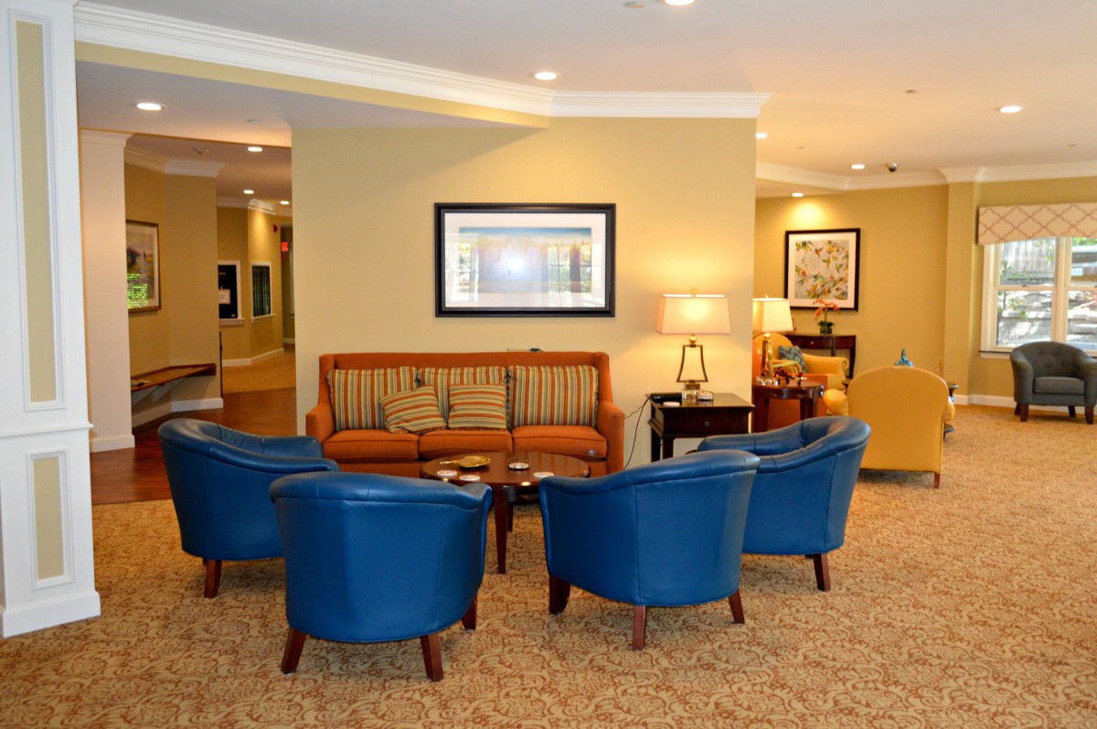 A cozy lobby seating area featuring blue chairs and a sofa arranged around a coffee table, with artwork adorning the walls.