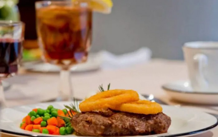 A delicious steak topped with onion rings, served with mixed vegetables and a glass of iced tea.