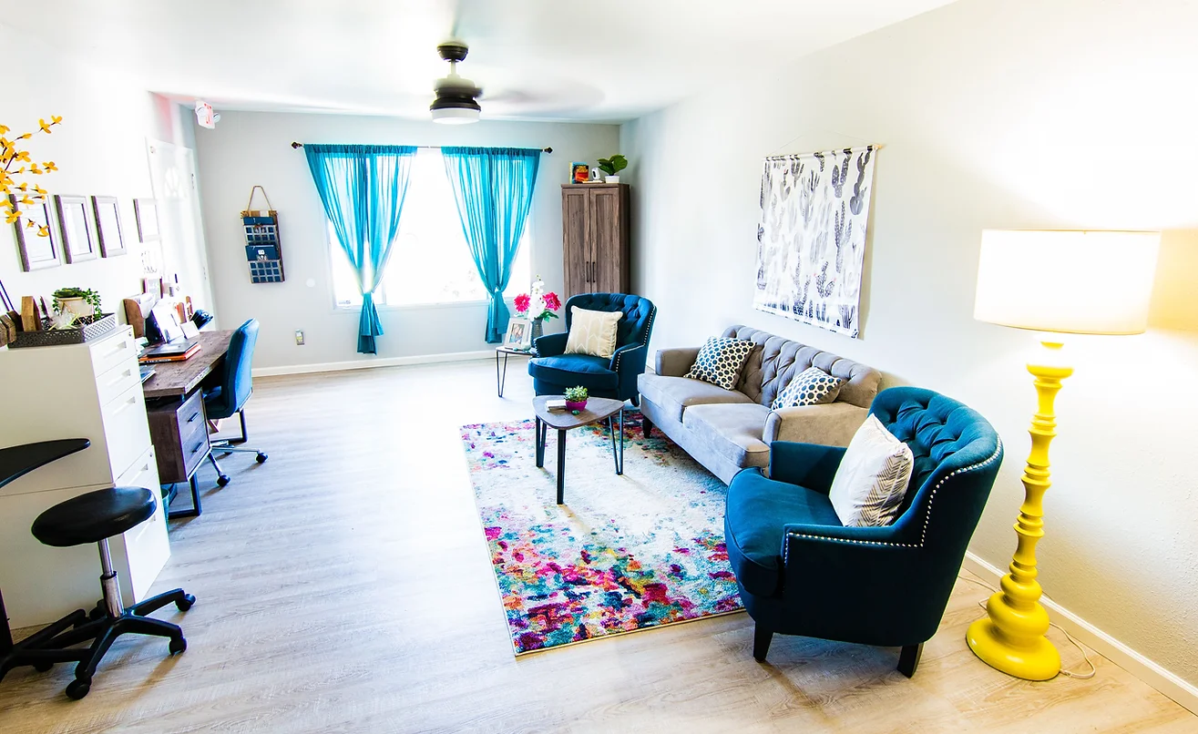 A modern living room featuring blue accents, including curtains and chairs, with a colorful rug enhancing the bright space.
