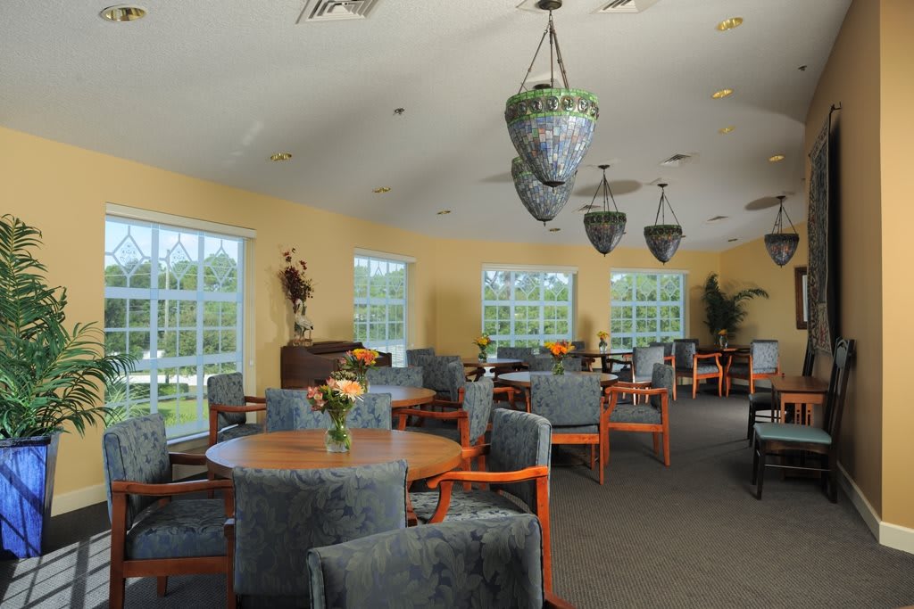 A well-lit dining area with multiple tables and chairs, featuring large windows and elegant lighting.