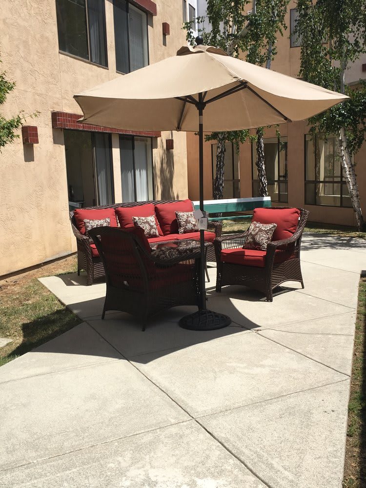 A sunny patio with red-cushioned outdoor furniture and an umbrella.