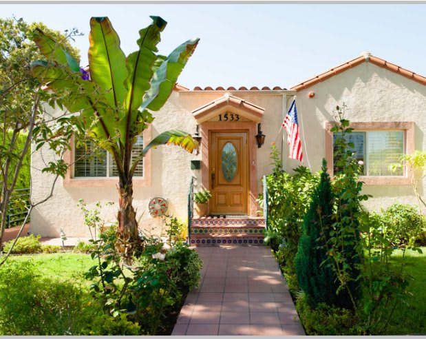 A charming house with a lush garden and palm tree in the front yard on a sunny day.