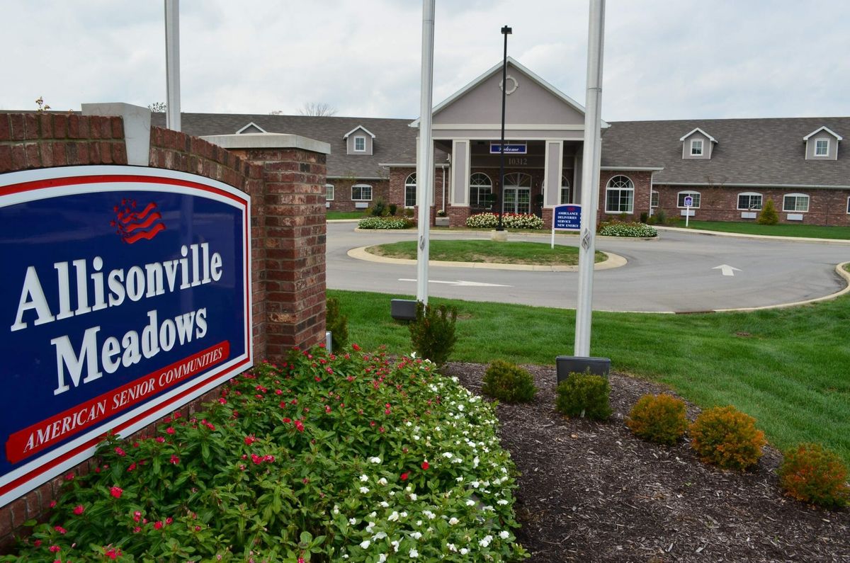 A landscaped entrance to a building with a prominent sign and flags.