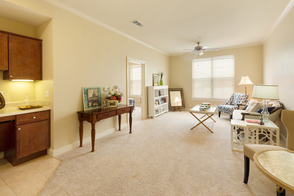 A cozy living room with neutral tones, featuring a sofa, coffee table, and ample natural light from a large window.