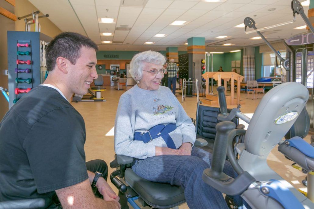 An elderly woman in a wheelchair engages with a caregiver in a rehabilitation center.
