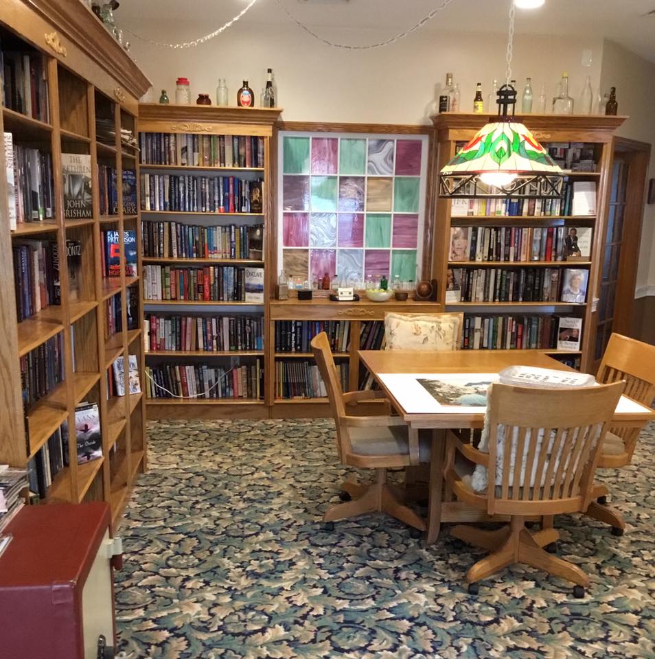 A cozy library corner with bookshelves, a wooden table, and chairs under a stained glass lamp.