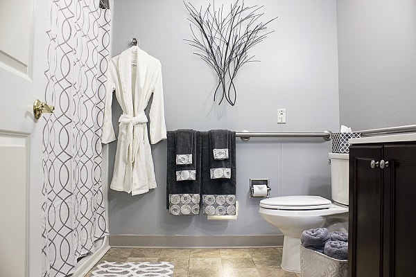 A modern bathroom with gray walls, featuring a white robe, black towels, and decorative wall art.