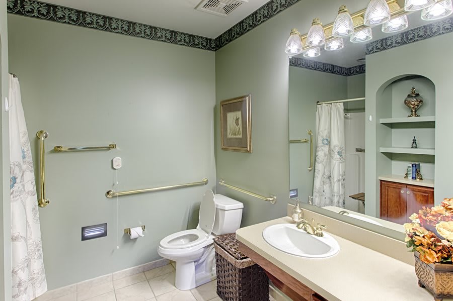 A well-lit bathroom featuring a toilet, sink, mirror, and shower with green painted walls.