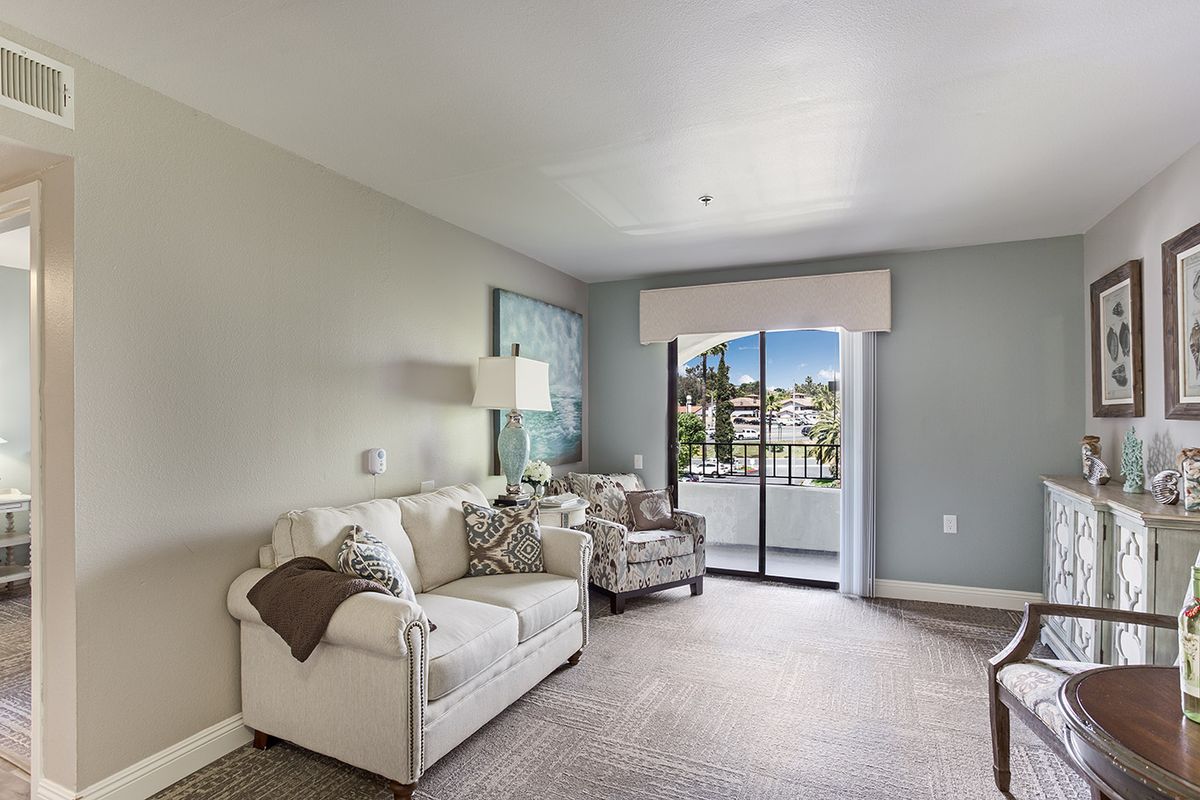 A modern living room with neutral colors featuring a comfortable sofa, armchairs, and a large window with a view outside.