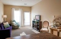 A cozy living room with a sofa, armchair, television, and large windows.