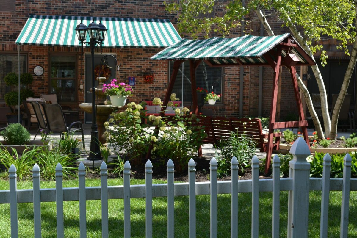 A cozy garden with a swing, colorful flowers, and a picket fence under striped awnings.