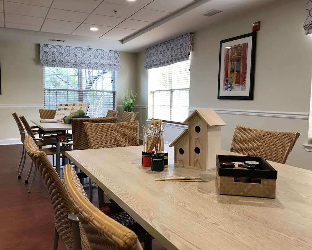 A cozy room with tables set up for crafting, featuring a birdhouse and art supplies.