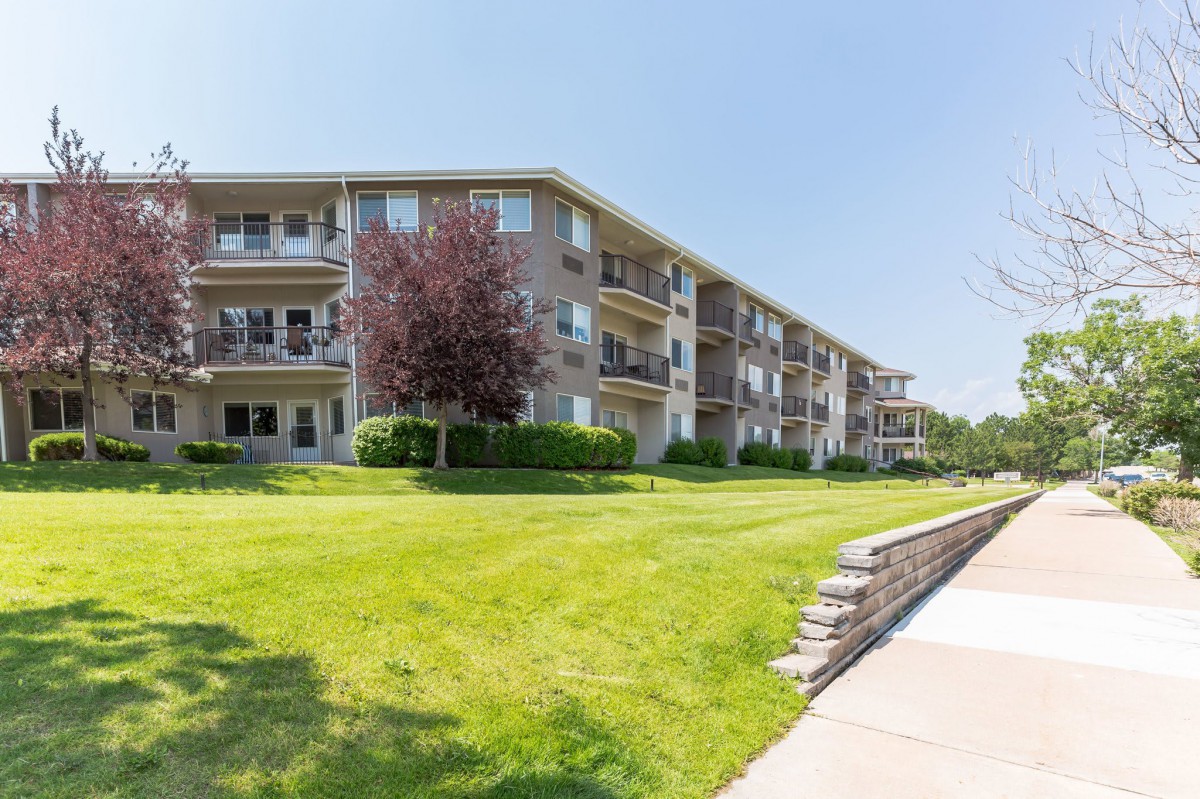 A low-rise apartment building with a well-maintained lawn and landscaping on a sunny day.