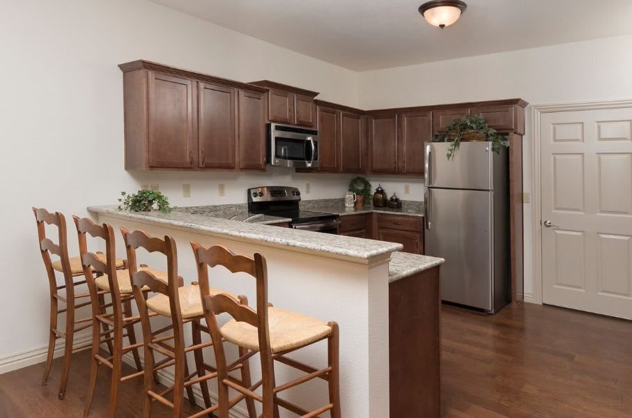 A modern kitchen with wooden cabinets, stainless steel appliances, and a breakfast bar with seating.