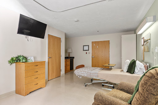 A modern hospital patient room featuring a bed, dresser, and wall-mounted TV.