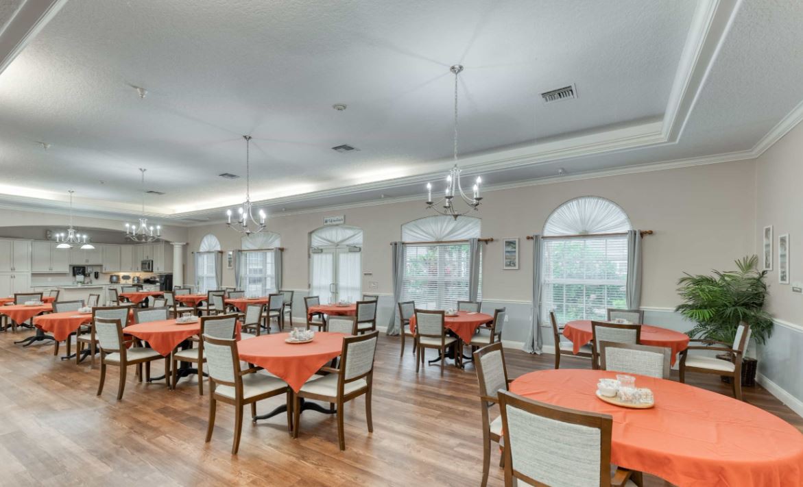 A spacious dining room with orange table settings and large windows.