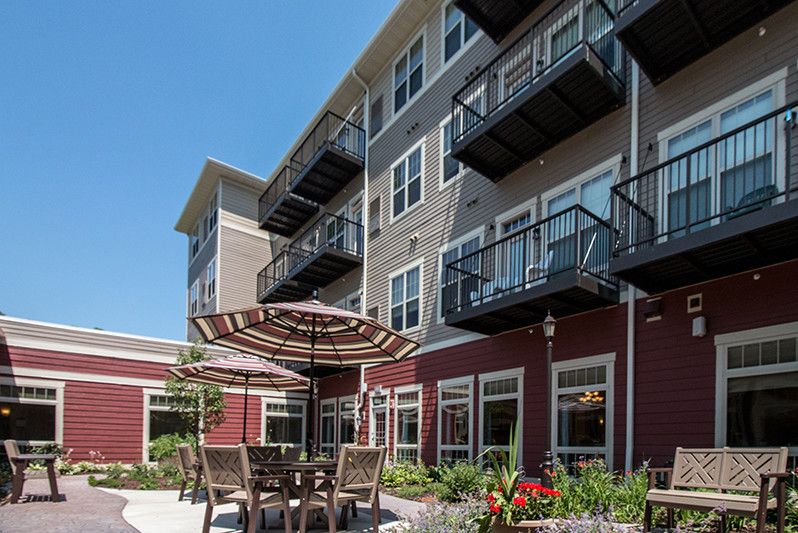 A modern apartment complex with balconies, featuring an outdoor patio area with tables, chairs, and umbrellas.