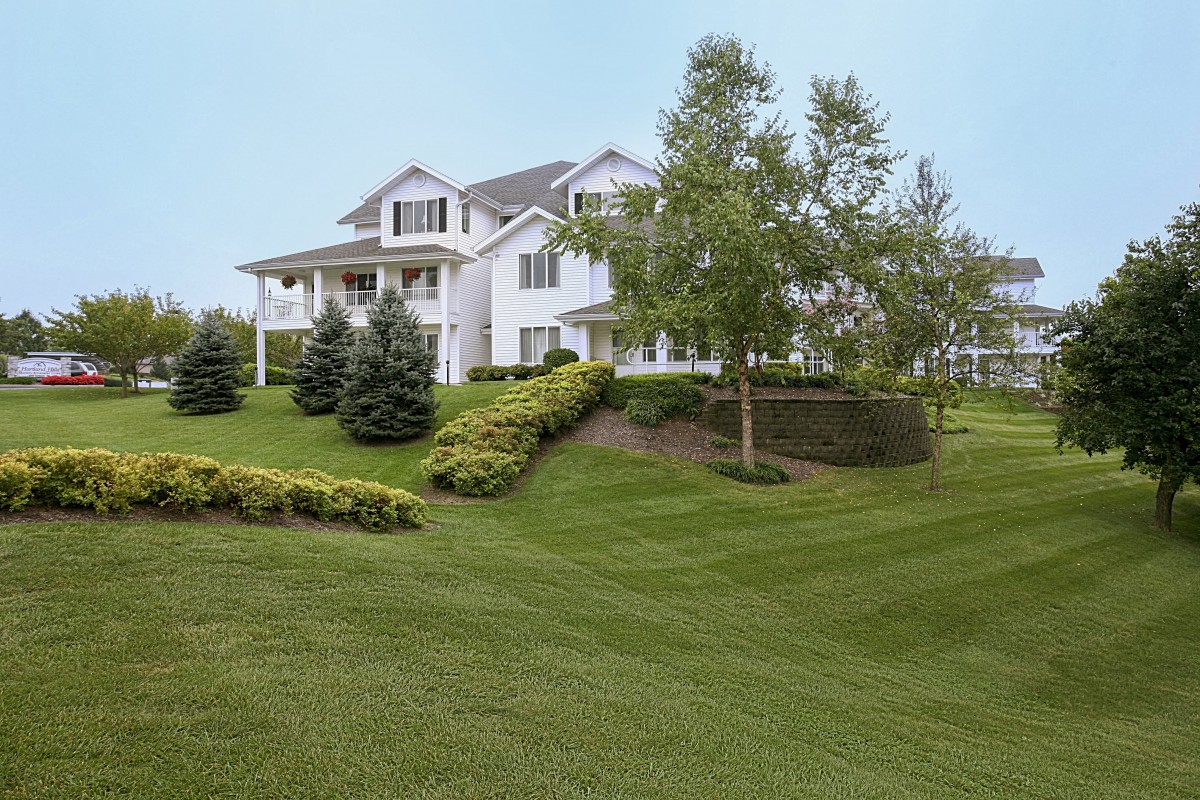 A large white suburban house with a well-manicured lawn and trees.