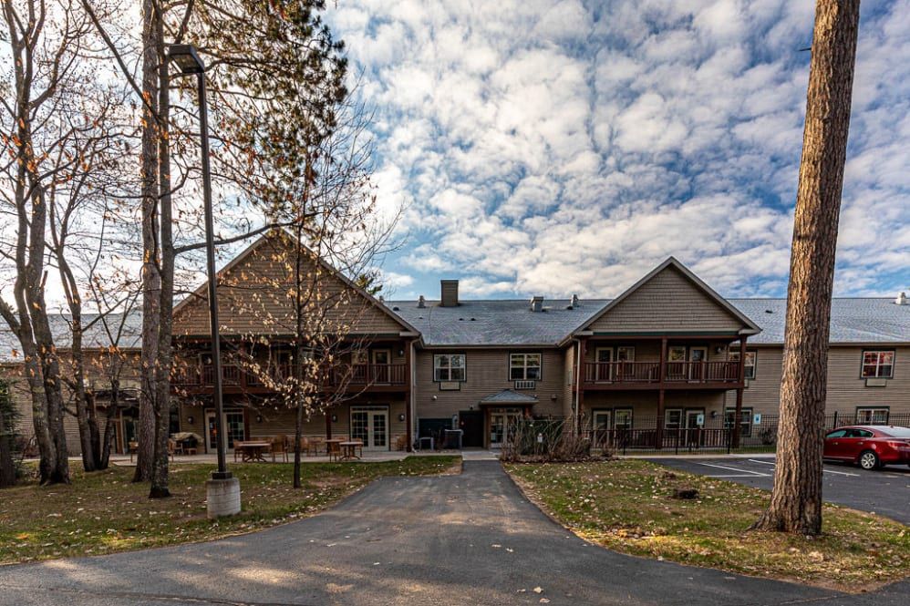 A large building with a driveway set against a backdrop of cloudy skies and surrounded by trees.