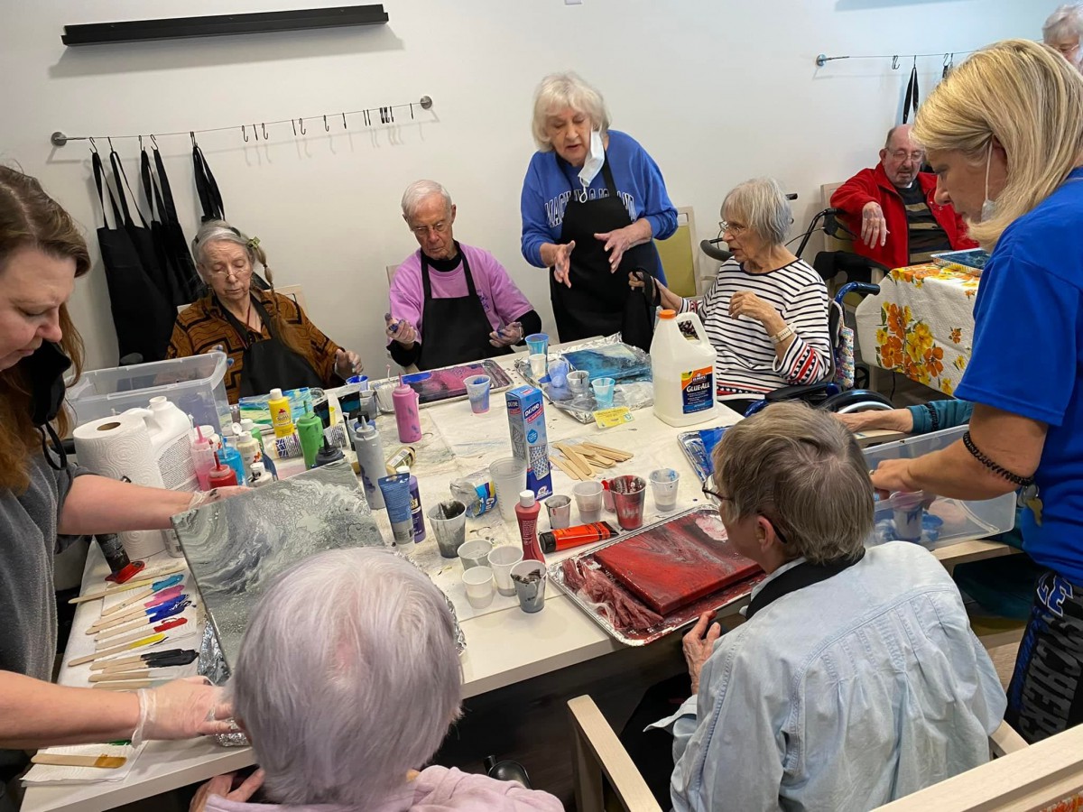 A group of seniors participating in an art class, with various painting supplies on the table.