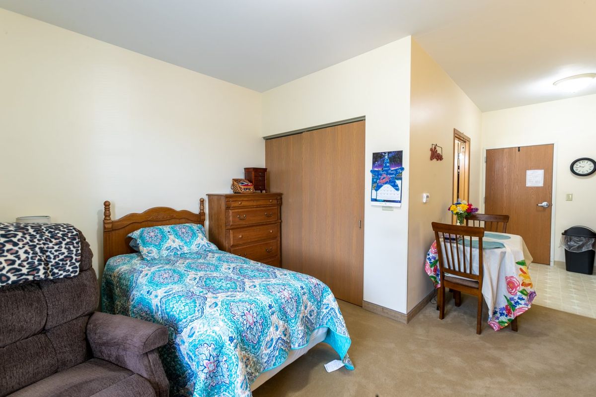 A cozy bedroom with a single bed and a dining area in view.