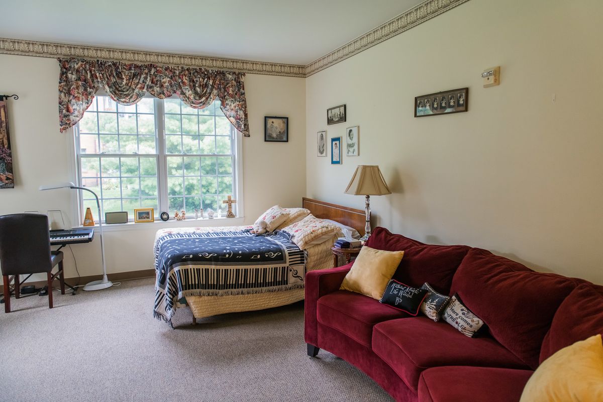 A cozy bedroom featuring a bed with patterned bedding, a red sofa with cushions, and a large window letting in natural light.