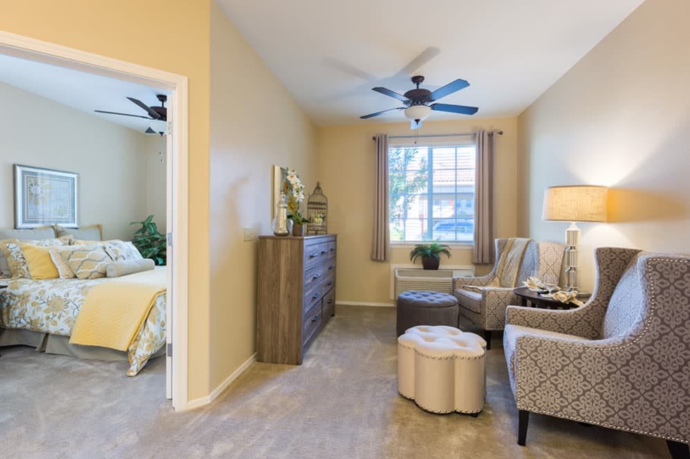 A cozy interior space with a living area and an adjacent bedroom, featuring comfortable seating, a dresser, and soft lighting.