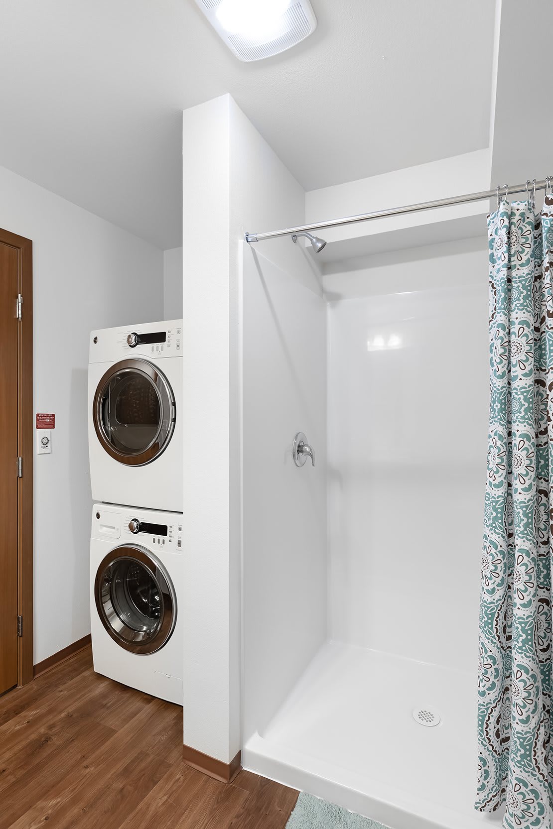 A compact laundry area with a stacked washer and dryer next to a shower in the bathroom.