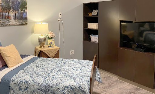 A cozy and modern bedroom featuring a neatly made bed with a blue patterned coverlet, a bedside lamp, and a stylish shelving unit.