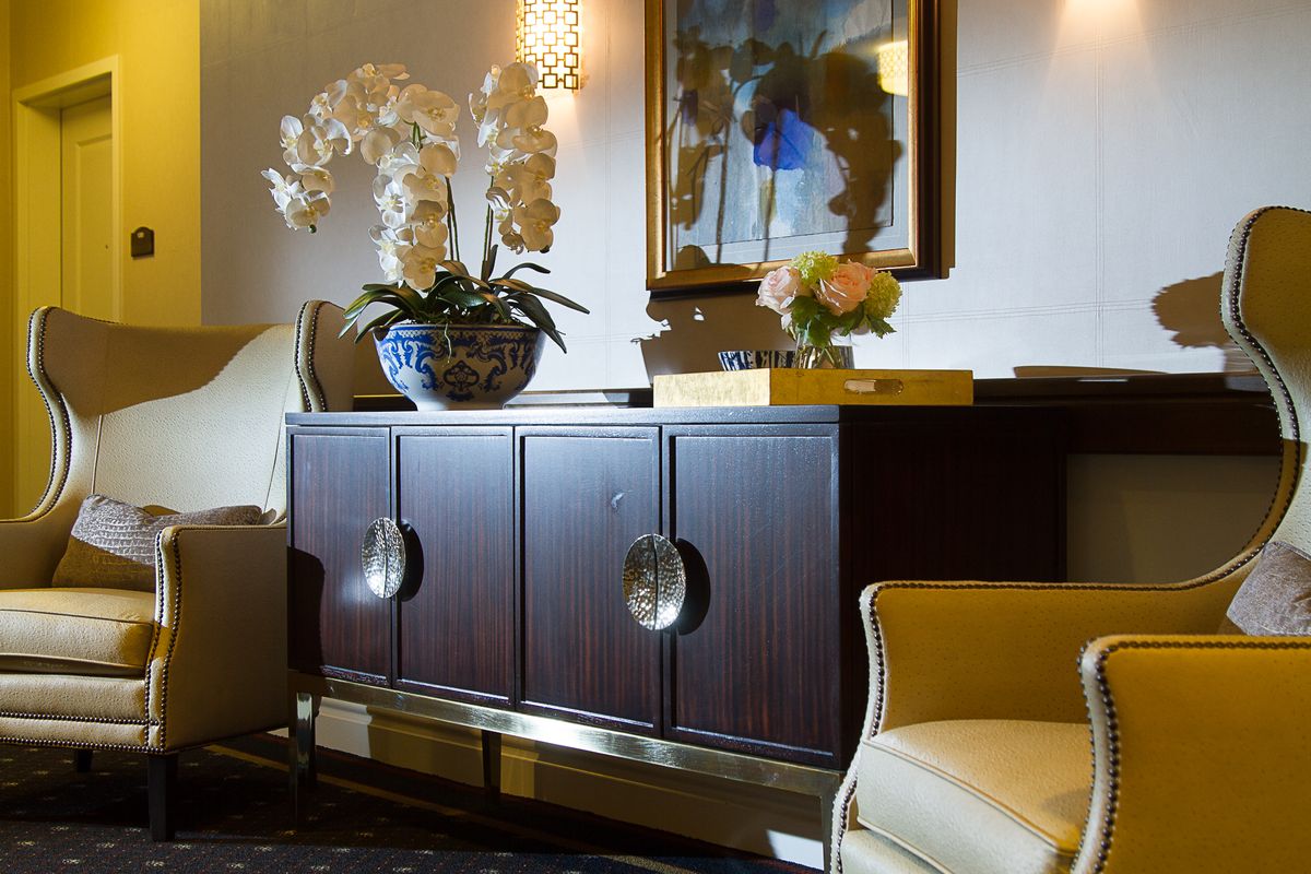 A stylish living room featuring a dark wood sideboard adorned with orchids and decorative items, complemented by artwork on the wall.