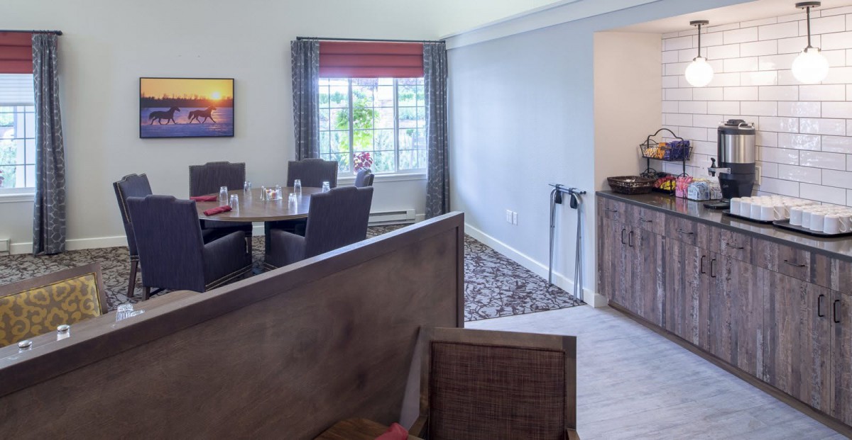 A cozy dining room featuring a table set with chairs, illuminated by natural light from a large window.