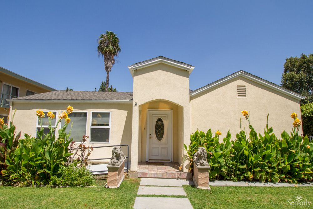A charming single-story house with a well-maintained lawn and garden under a clear blue sky.