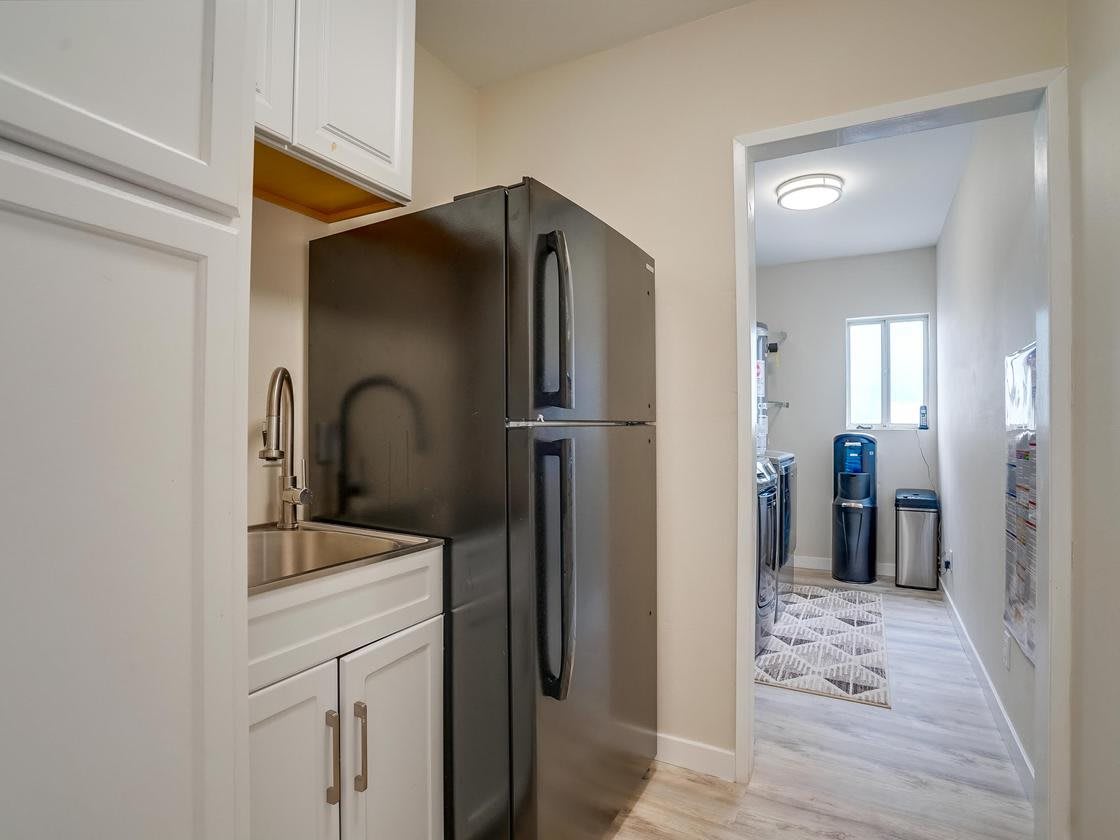 A modern kitchen with a black refrigerator, white cabinets, and an adjoining laundry room.