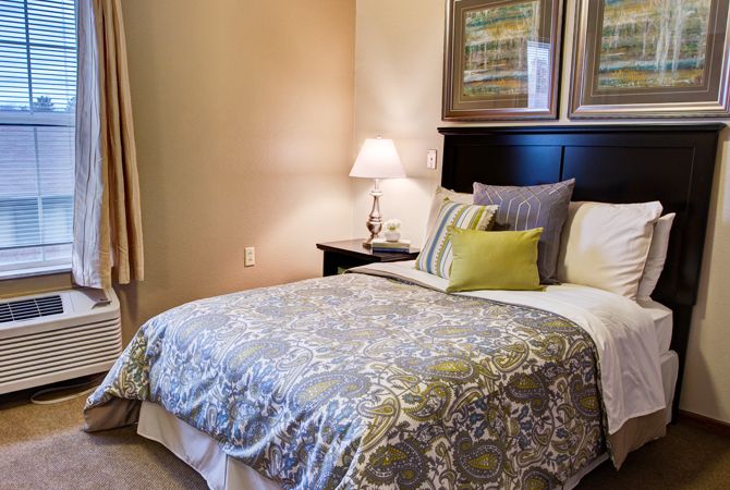 A cozy bedroom with a neatly made bed, decorative pillows, and a bedside lamp.