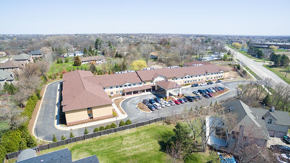 Aerial view of a large building with a parking lot in a suburban setting surrounded by greenery.