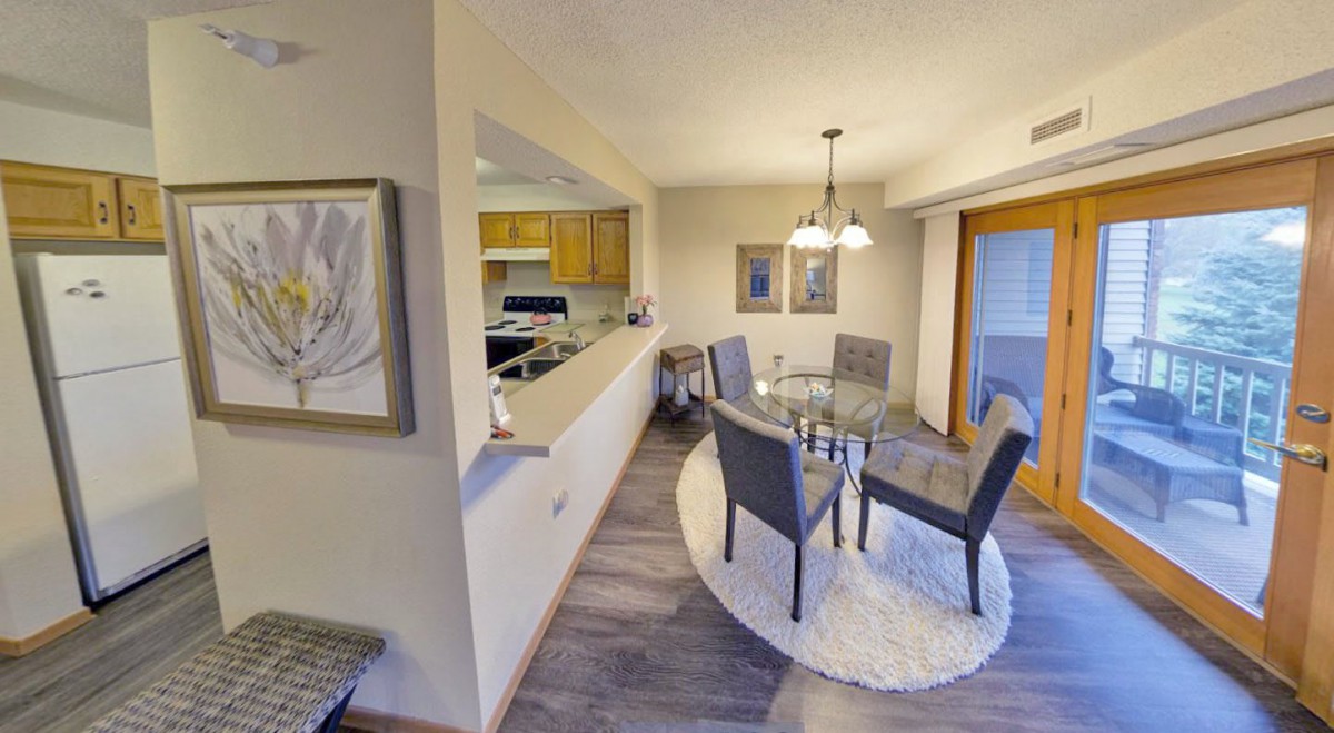 A modern dining area with an open layout leading to the kitchen, featuring a round glass table and upholstered chairs.