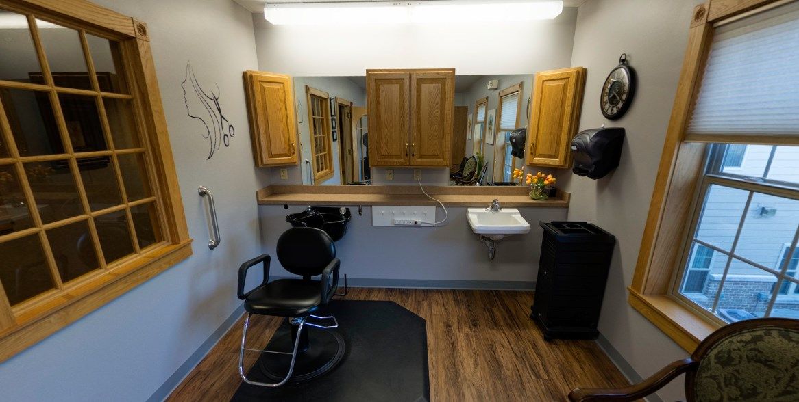 A compact barber shop interior featuring a styling chair, mirror, wooden cabinets, and a sink.