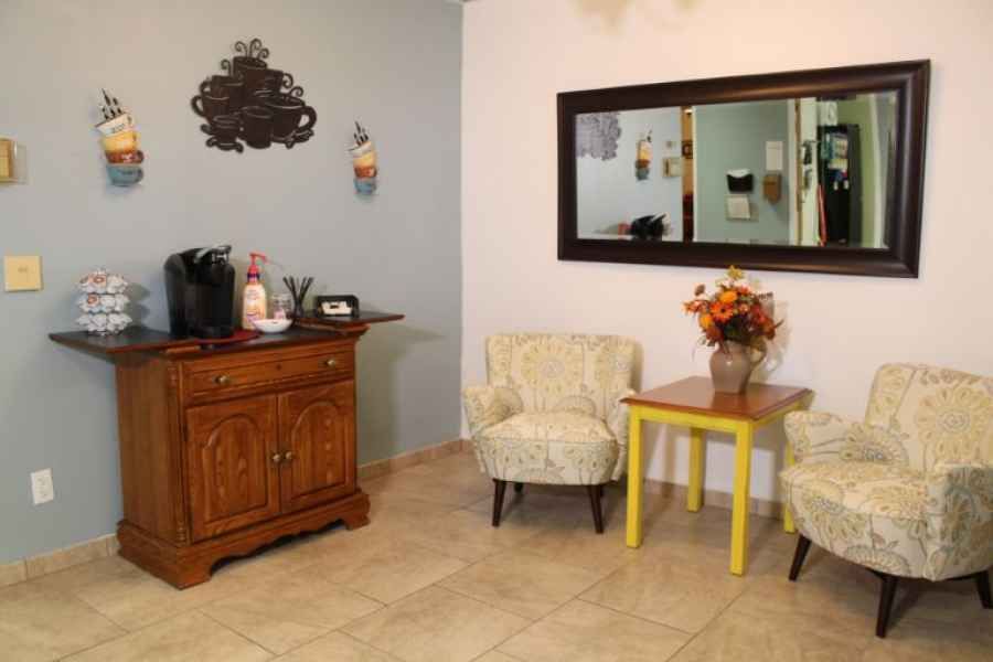 A cozy waiting room with two chairs, a yellow table, and decorative elements such as a mirror and flowers.